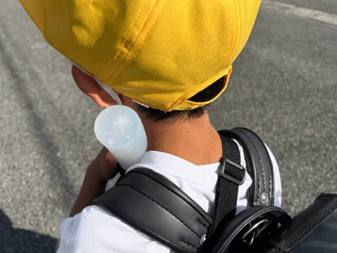 首元に氷嚢を当てて暑さ対策をしながら登校する小学生